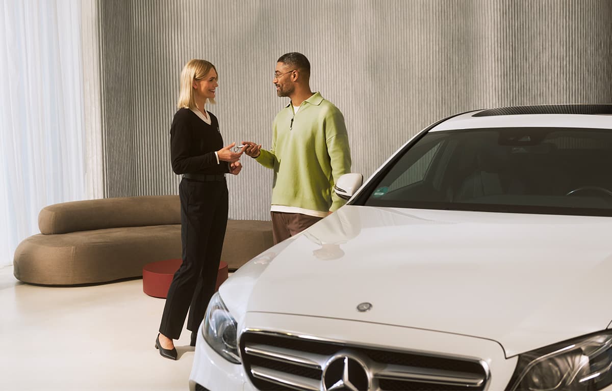 Ein Mitarbeiter eines Autohauses übergibt einen Fahrzeugschlüssel an einen Kunden.