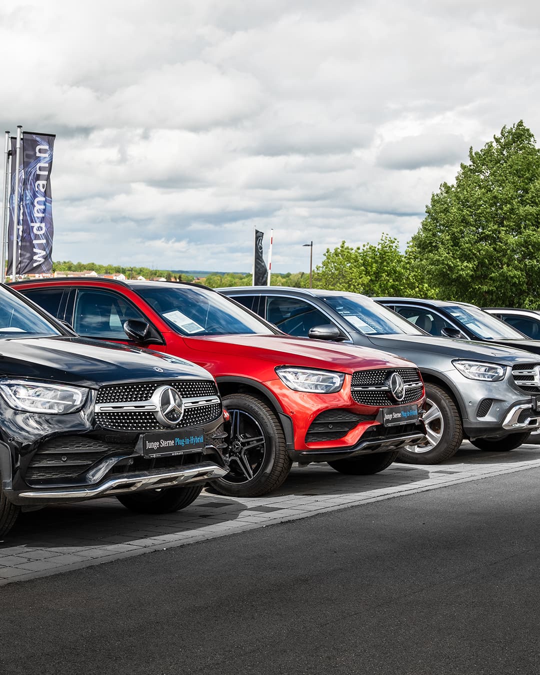 Vor einer dunklen Merceces-Benz Motorhaube wid ein Fahrzeugschlüssel übergeben.