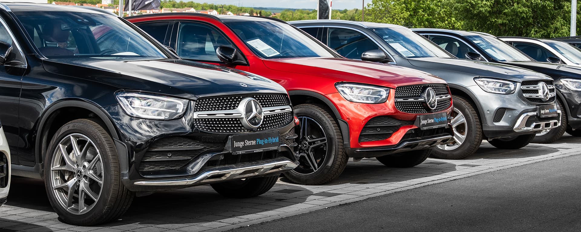 Vor einer dunklen Merceces-Benz Motorhaube wid ein Fahrzeugschlüssel übergeben.