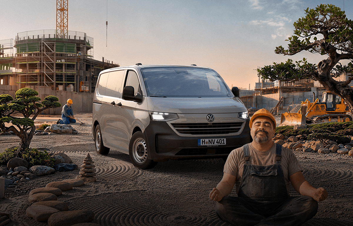 Ein grauer Volkswagen Transporter steht auf einer Baustelle, während im Vordergrund ein Bauarbeiter im Schneidersitz meditiert.