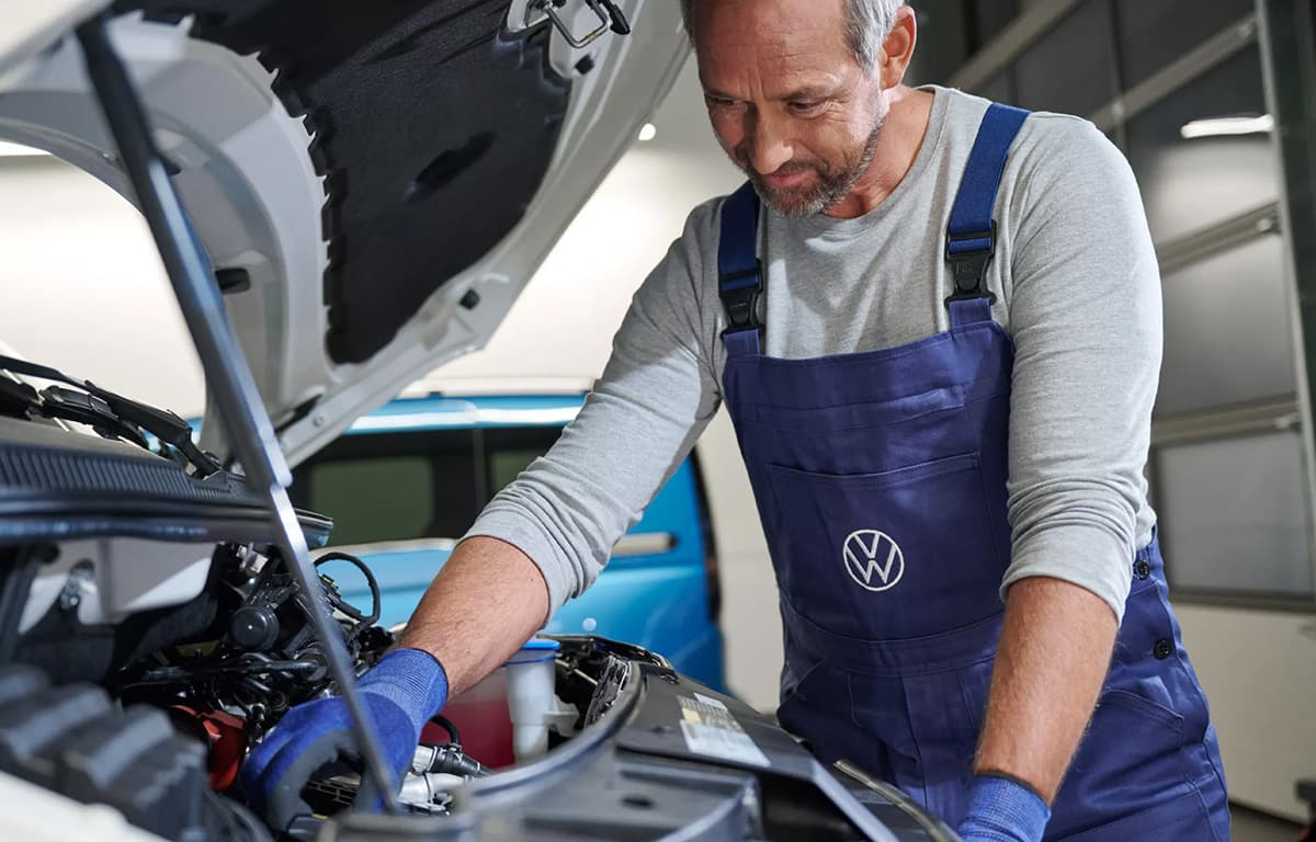 Ein Volkswagen Werkstattmitarbeiter arbeitet an einer geöffneten Motorhaube.