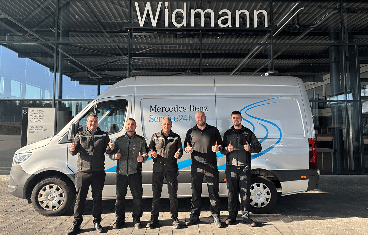 Fünf Service-Mitarbeiter stehen vor einem Mercedes-Benz Transporter vor dem Autohaus und zeigen mit Daumen nach oben ihre Zufriedenheit.