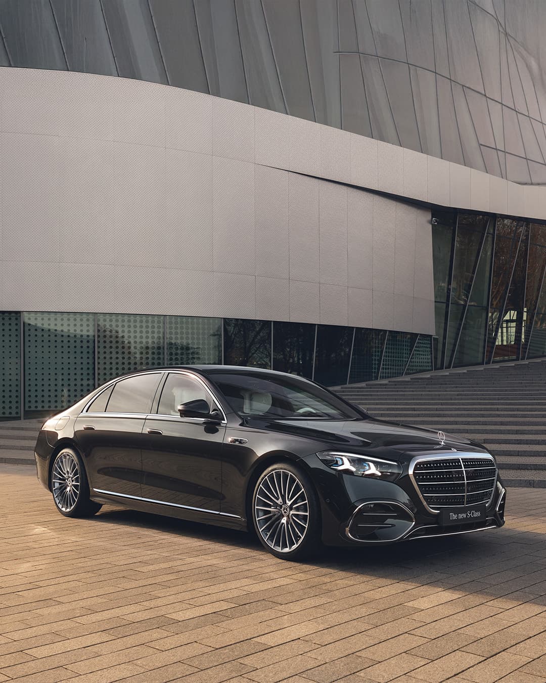 Eine schwarze S-Klasse steht vor einem modernen Gebäude mit breiten Stufen.