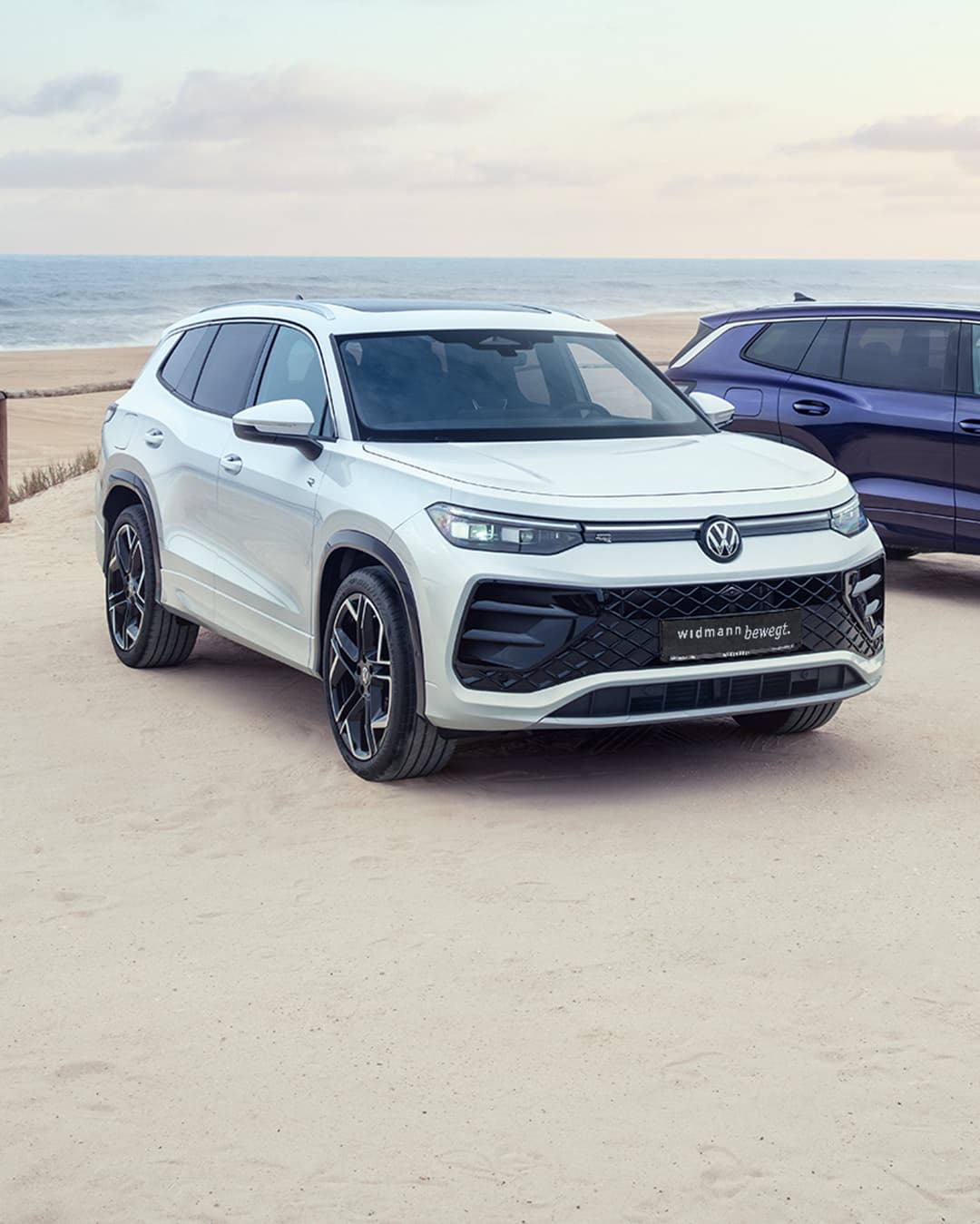 Ein weißer und ein blauer Volkswagen Tayron an einem Strand.