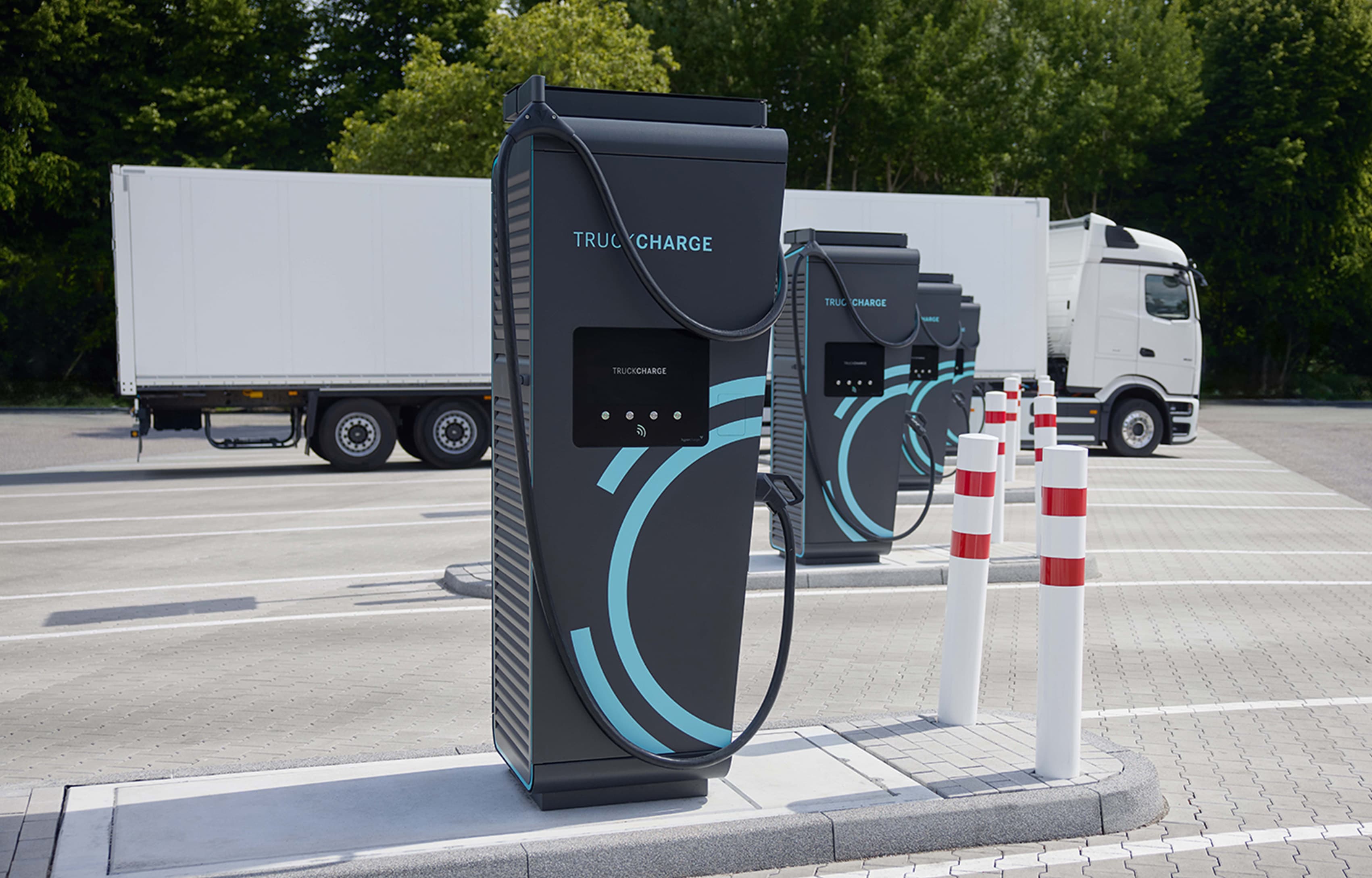 Ladestationen für elektrische Nutzfahrzeuge auf einem Parkplatz mit mehreren Lkw im Hintergrund.