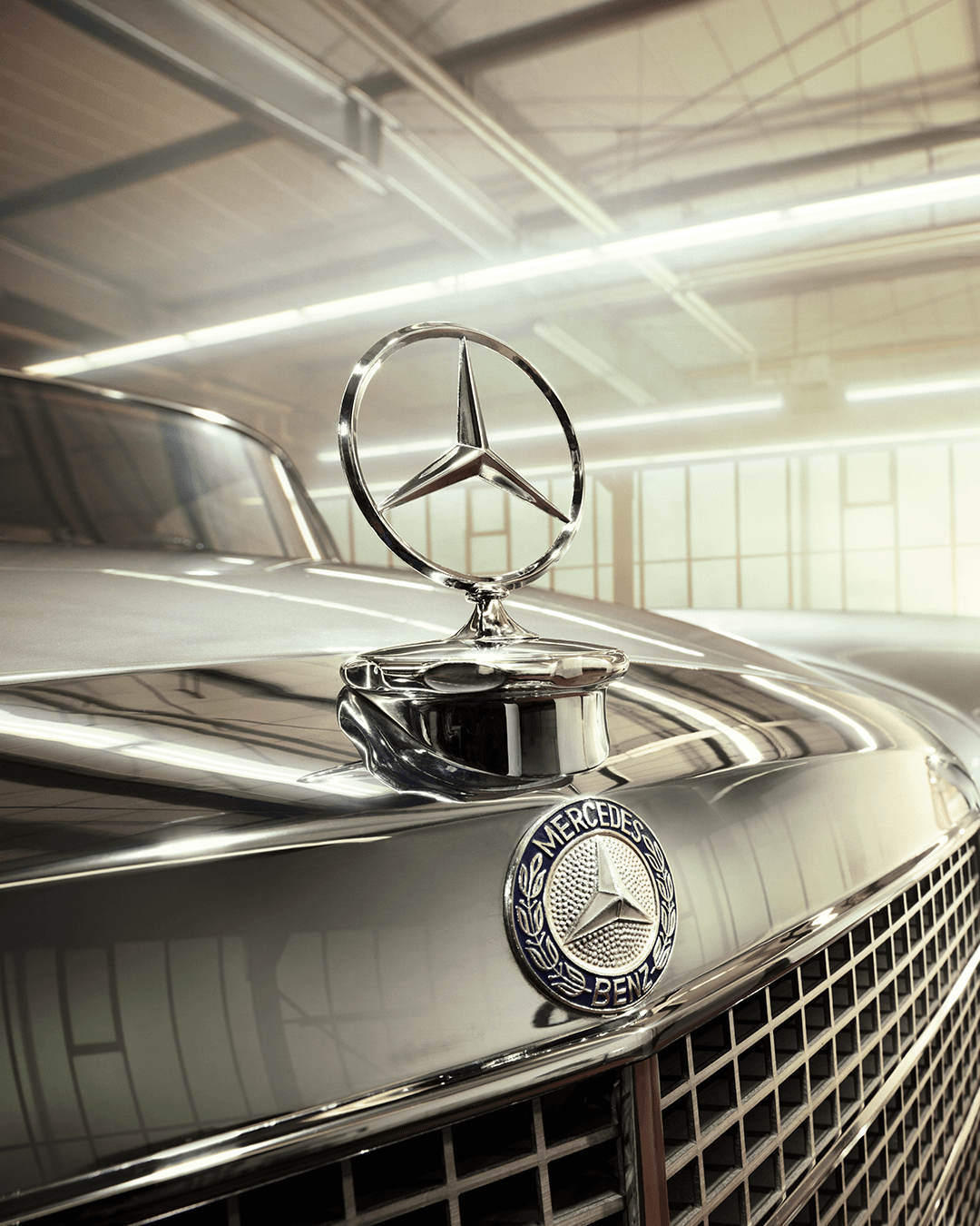 Nahaufnahme eines klassischen Mercedes-Benz mit glänzender Motorhaube und Stern-Emblem in heller Werkhalle.