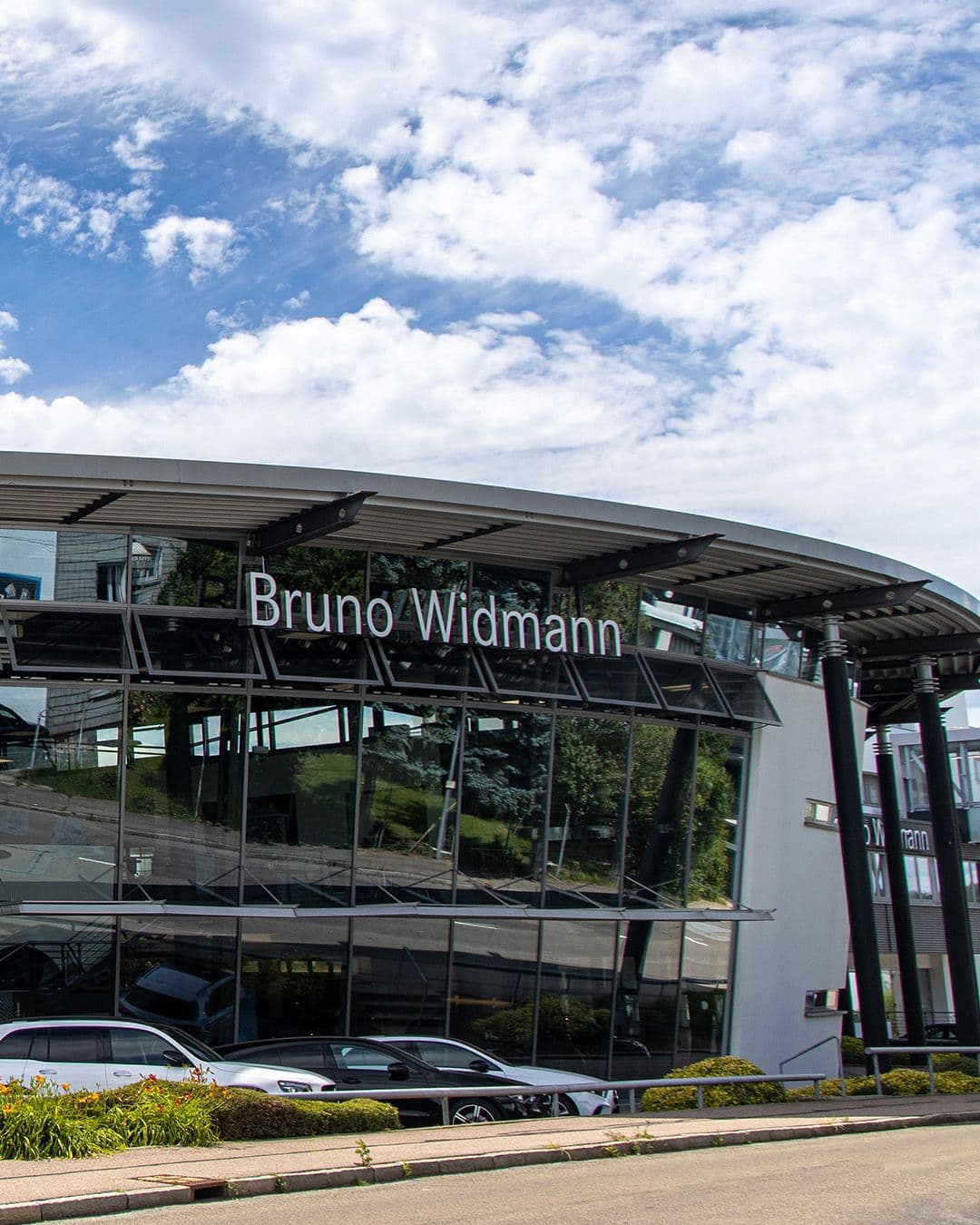 Das Bild zeigt unser Mercedes-Benz Autohaus von außen, vor dem mehrere Fahrzeuge geparkt sind.
