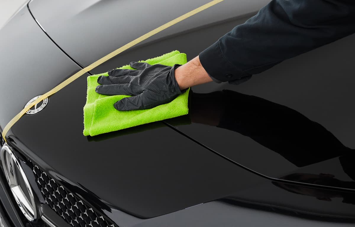 Die Hand eines Aufbereiters poliert eines schwarze Motorhaube.