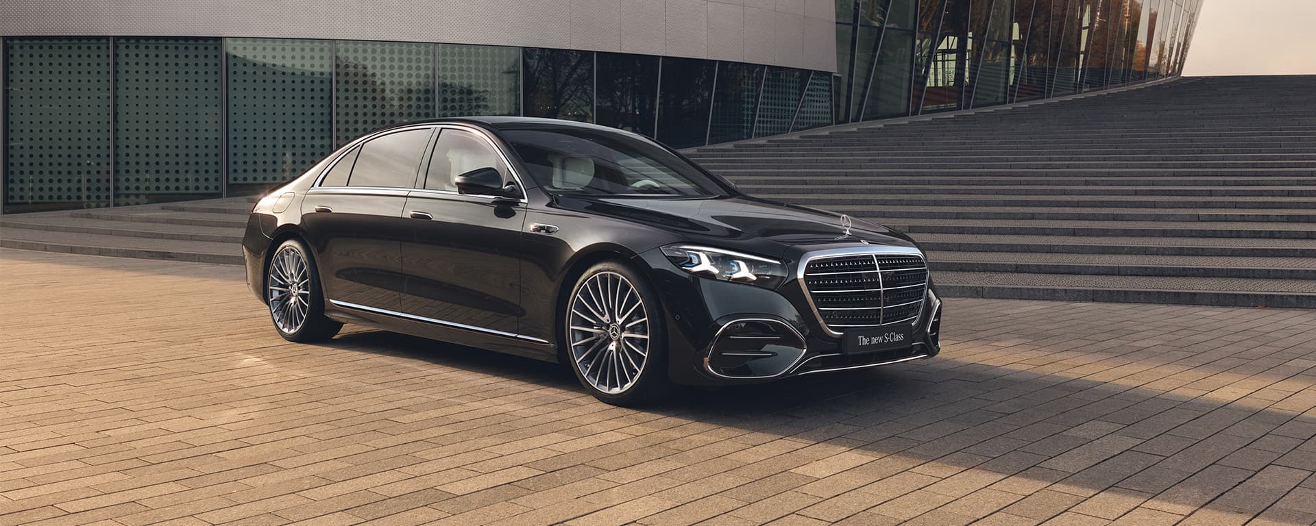 Eine schwarze S-Klasse steht vor einem modernen Gebäude mit breiten Stufen.