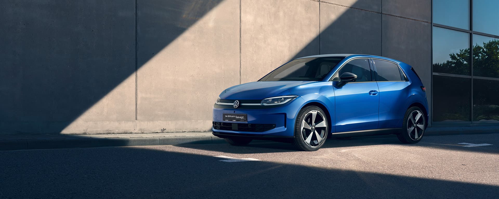 Ein blauer Kompaktwagen steht im Sonnenlicht vor einer modernen Betonwand, teilweise im Schatten.