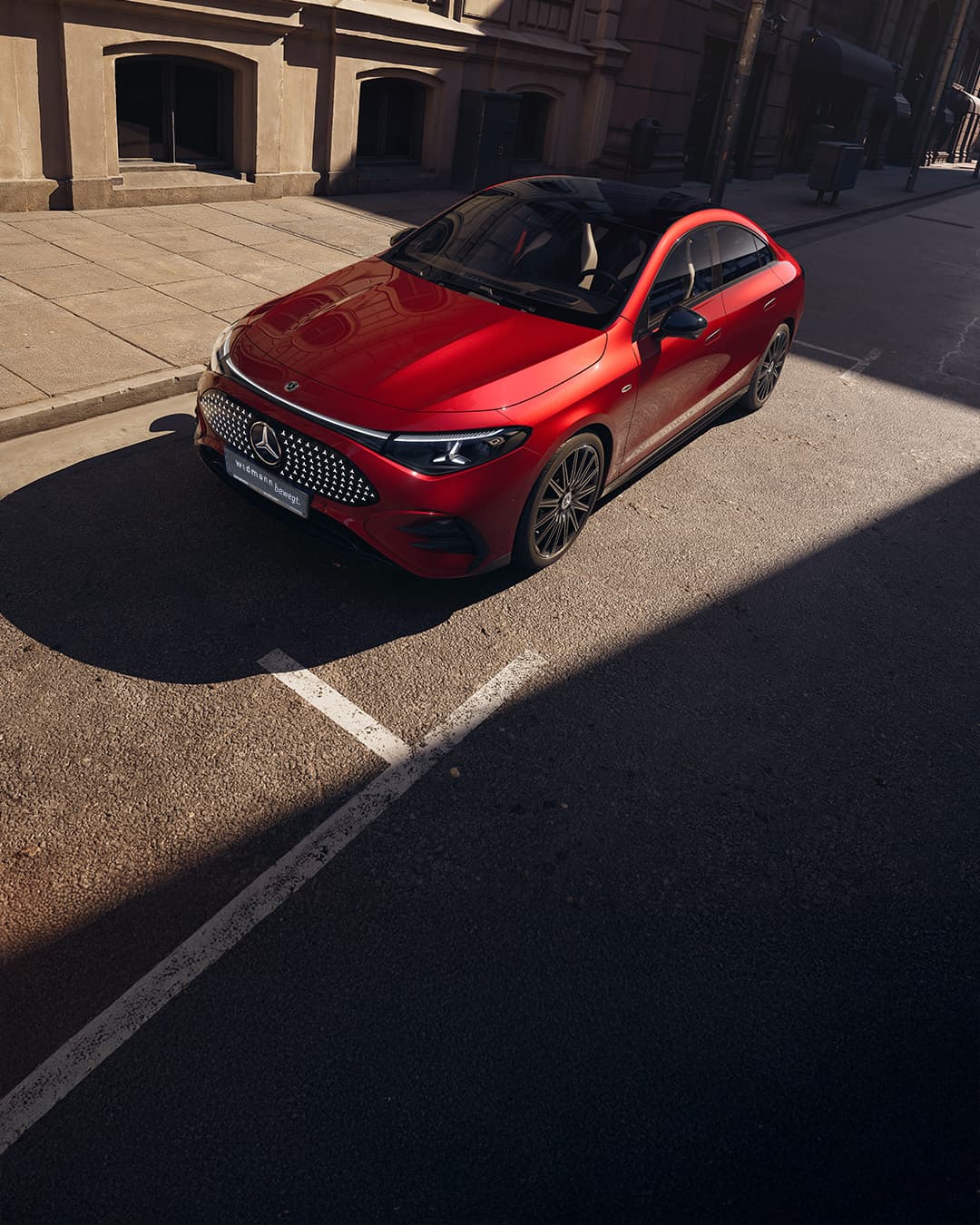 Ein roter CLA steht schräg auf einer ruhigen Stadtstraße neben einem Gebäude bei Tageslicht.