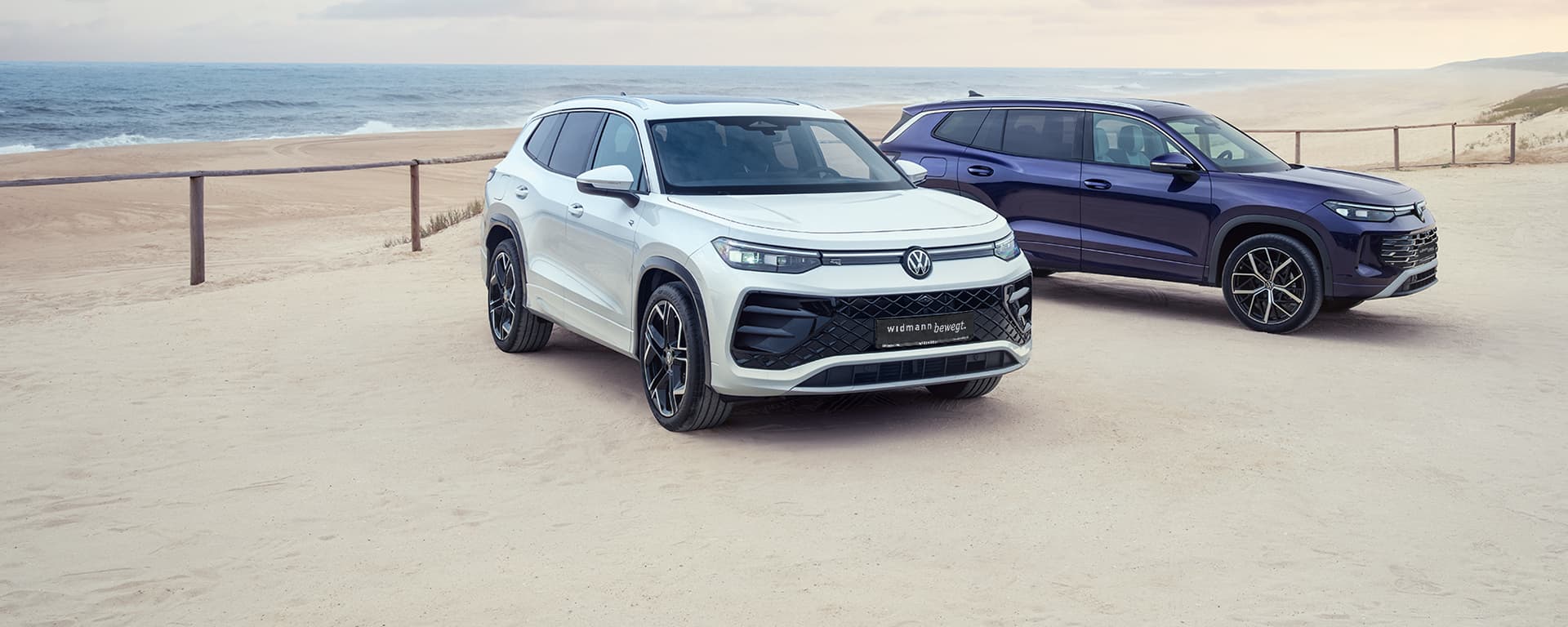Ein weißer und ein blauer Volkswagen Tayron an einem Strand.