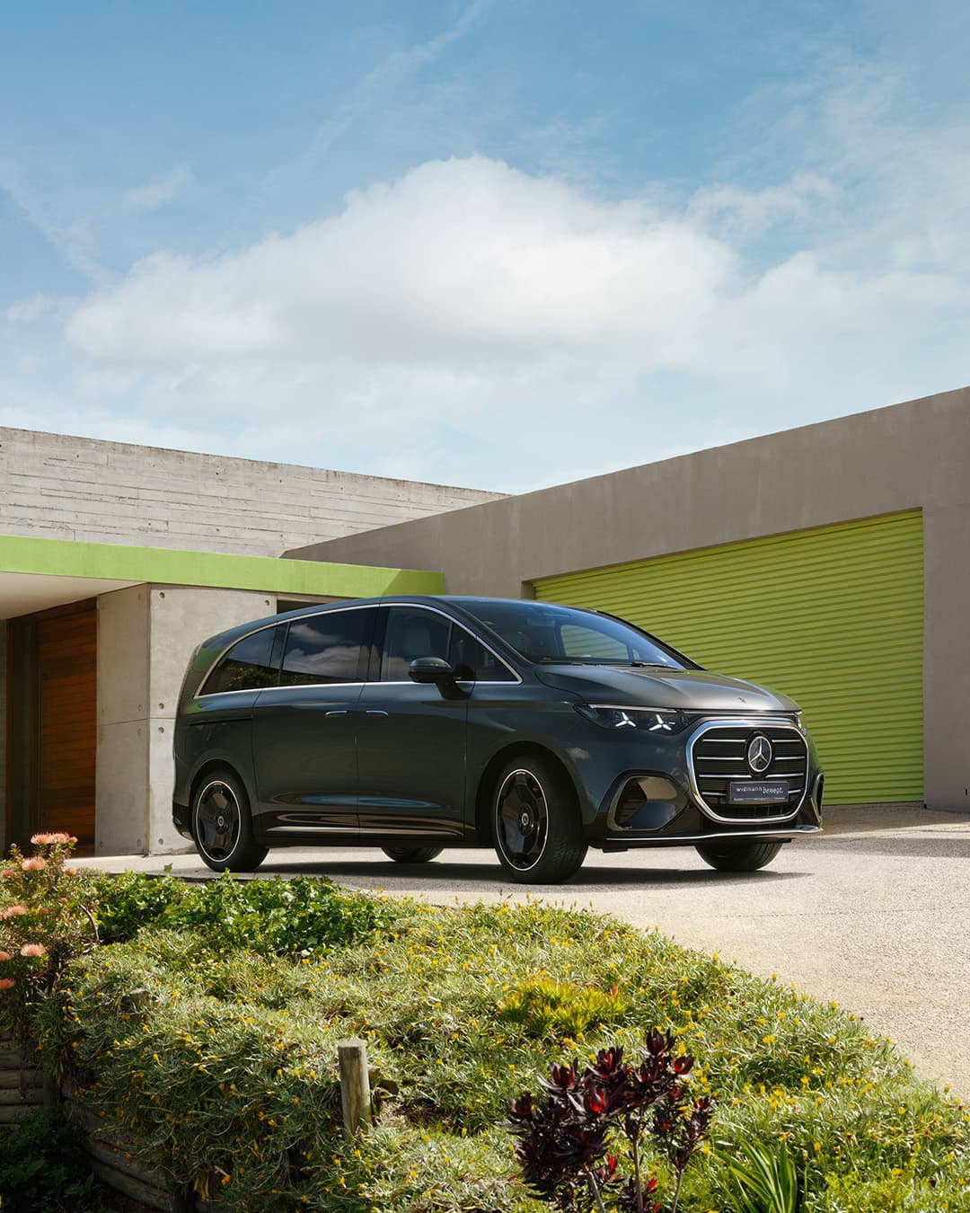 Ein dunkler Van steht vor einem modernen Gebäude mit grünem Tor.