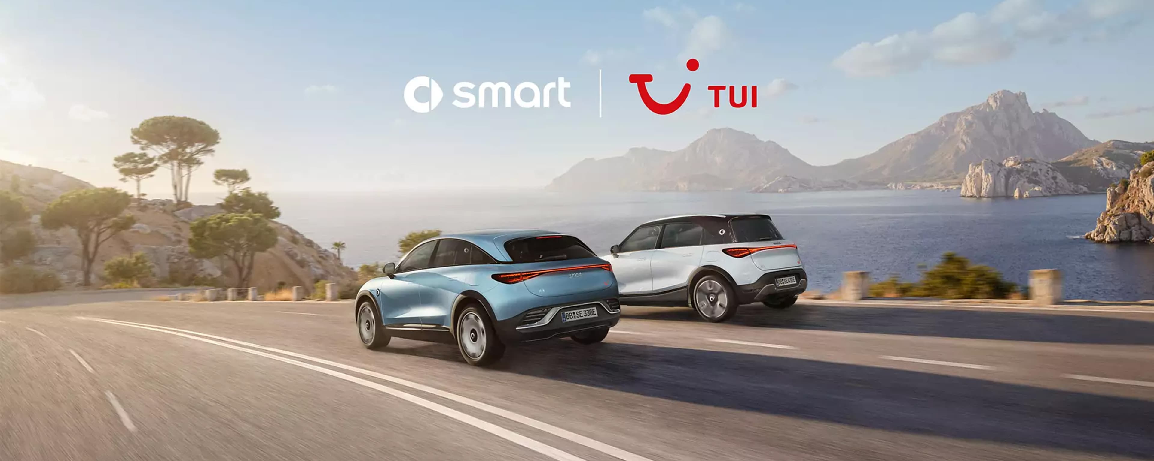 Zwei smart-Fahrzeuge fahren auf einer Küstenstraße, mit dem Meer im Hintergrund.