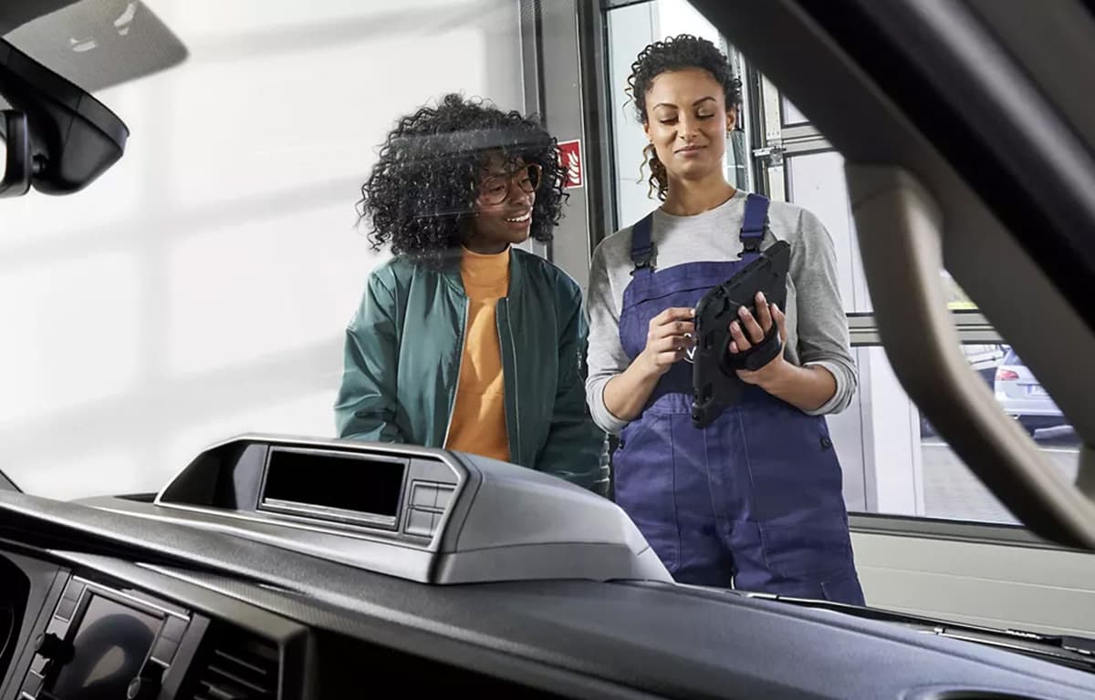 Eine Volkswagen Werkstatt Mitarbeiterin und eine Kundin an einem Fahrzeug.