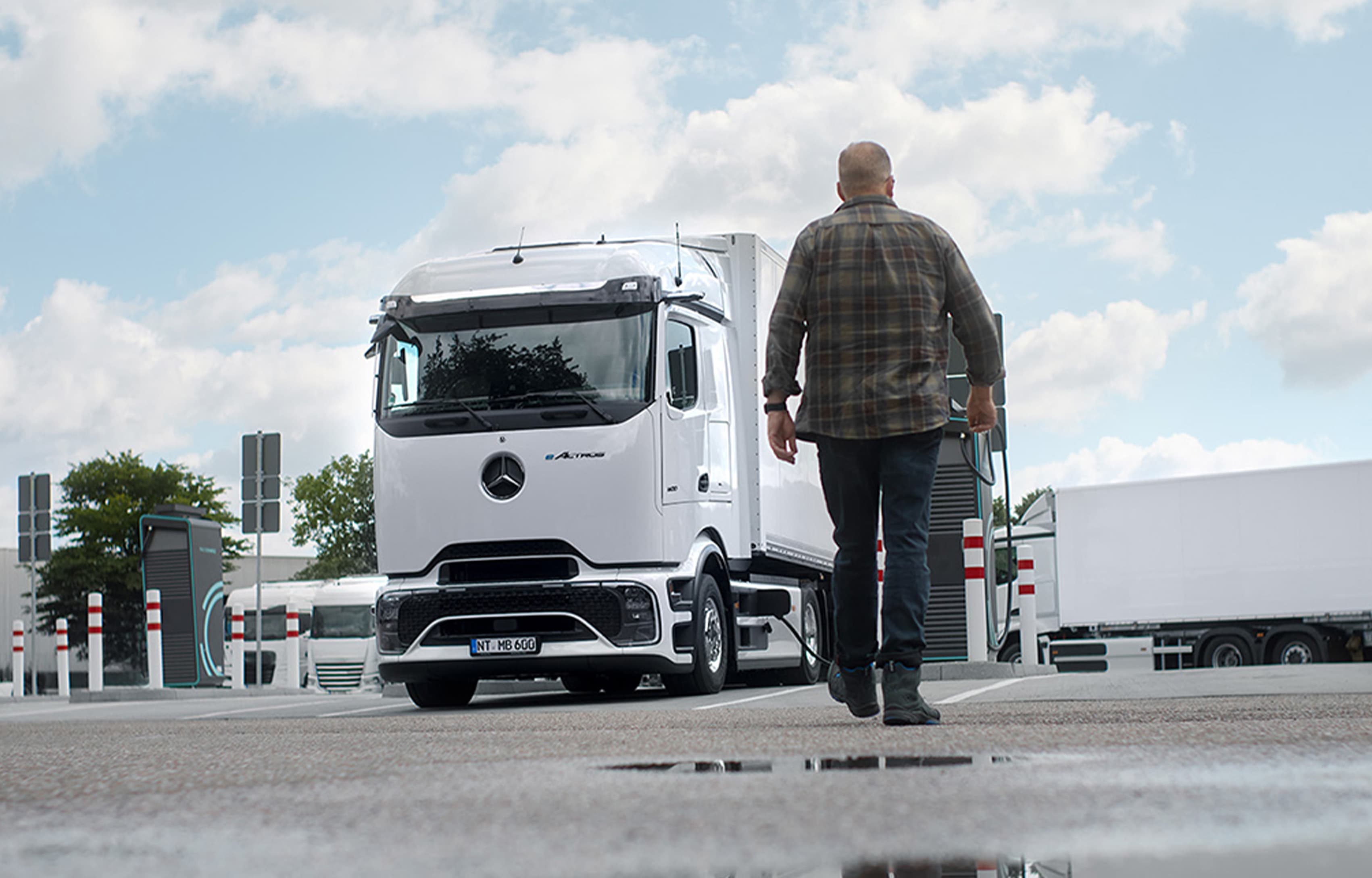 Person geht über einen Ladepark zu einem elektrischen Mercedes-Benz Lkw, der an einer Schnellladestation geladen wird.