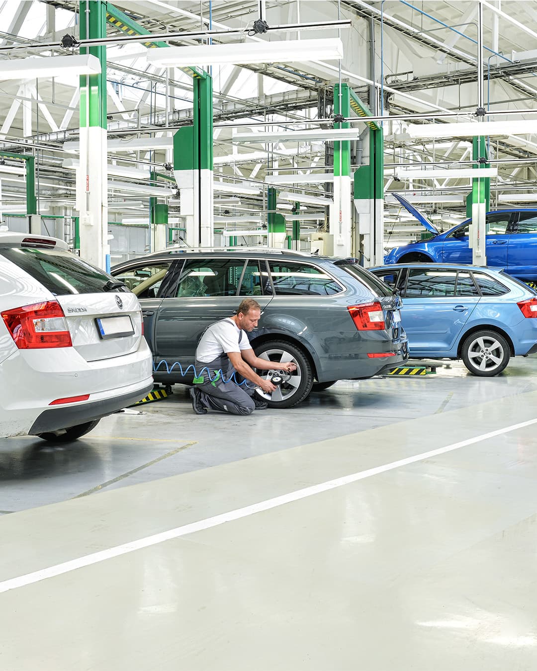 Mehrere ŠKODA Fahrzeuge stehen in einer hellen Werkstatt, während Mechaniker Wartungs- und Reparaturarbeiten durchführen.