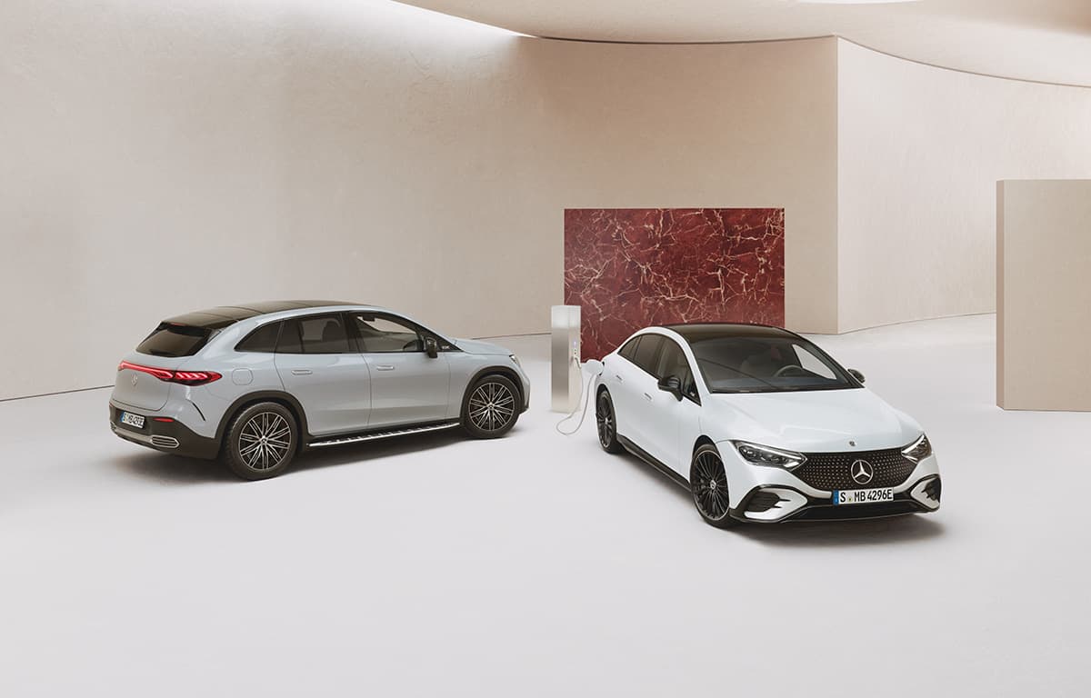 Zwei moderne Mercedes-Elektroautos stehen in einem hellen Raum, eines davon ist an einer Ladestation angeschlossen.
