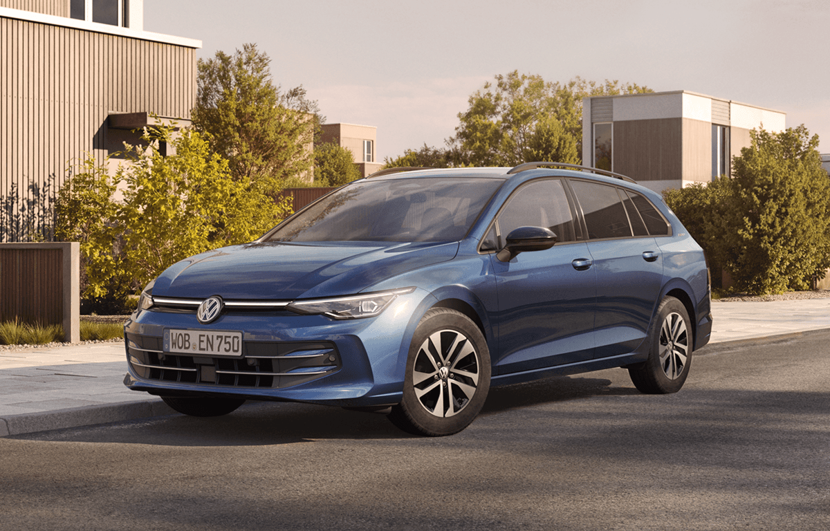 Ein blauer elektrischer Kombi (VW ID.7 GTX) steht auf einer hellen Fläche vor einer ruhigen Küstenlandschaft unter leicht bewölktem Himmel.