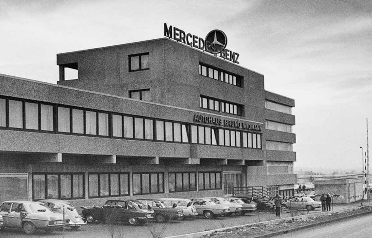 Ein Schwarz-Weiß-Bild eines Autohauses von außen mit Fahrzeugen davor.