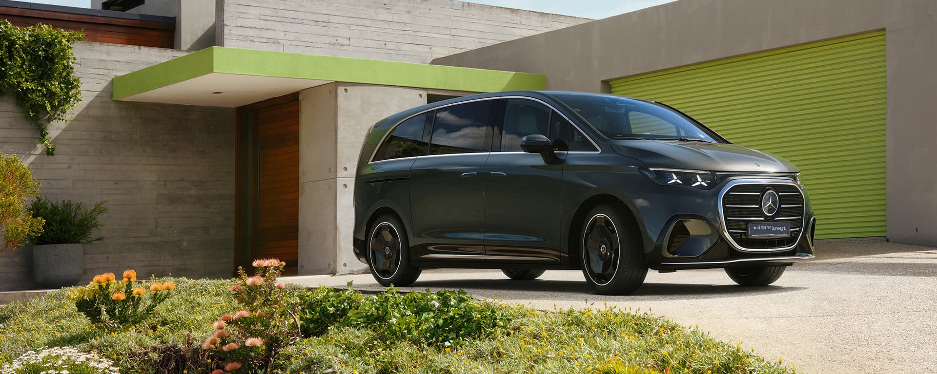 Ein dunkler Van steht vor einem modernen Gebäude mit grünem Tor.