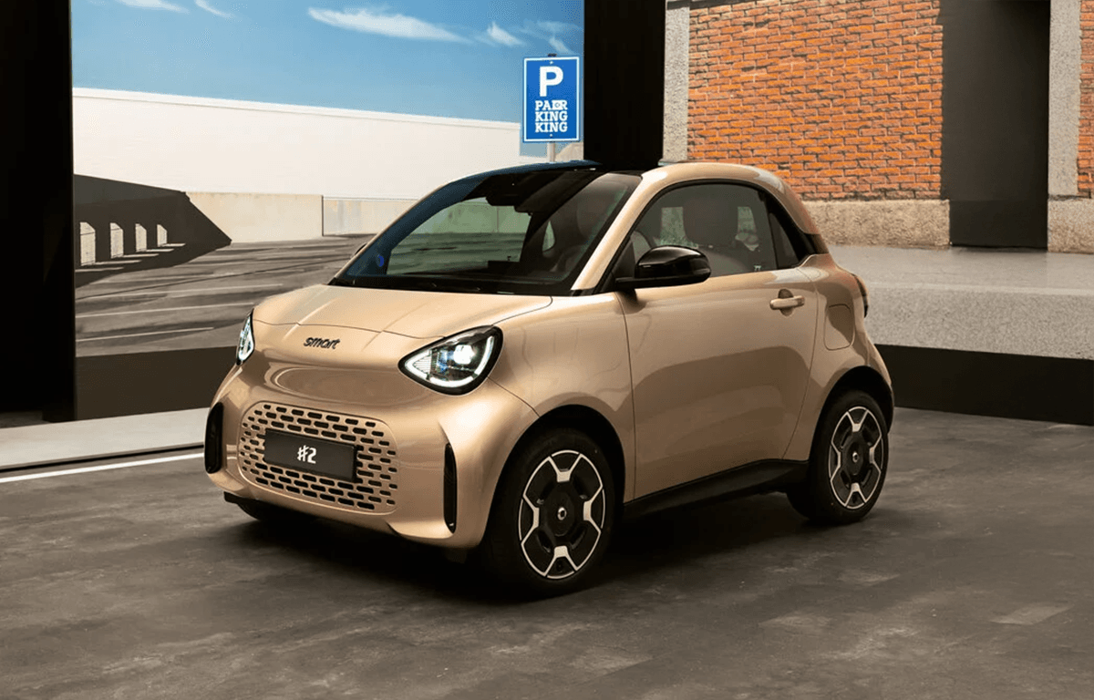 Goldfarbener smart #2 mit schwarzem Dach und markanten Leichtmetallfelgen in der Front- und Seitenansicht vor einer modernen Gebäudekulisse.