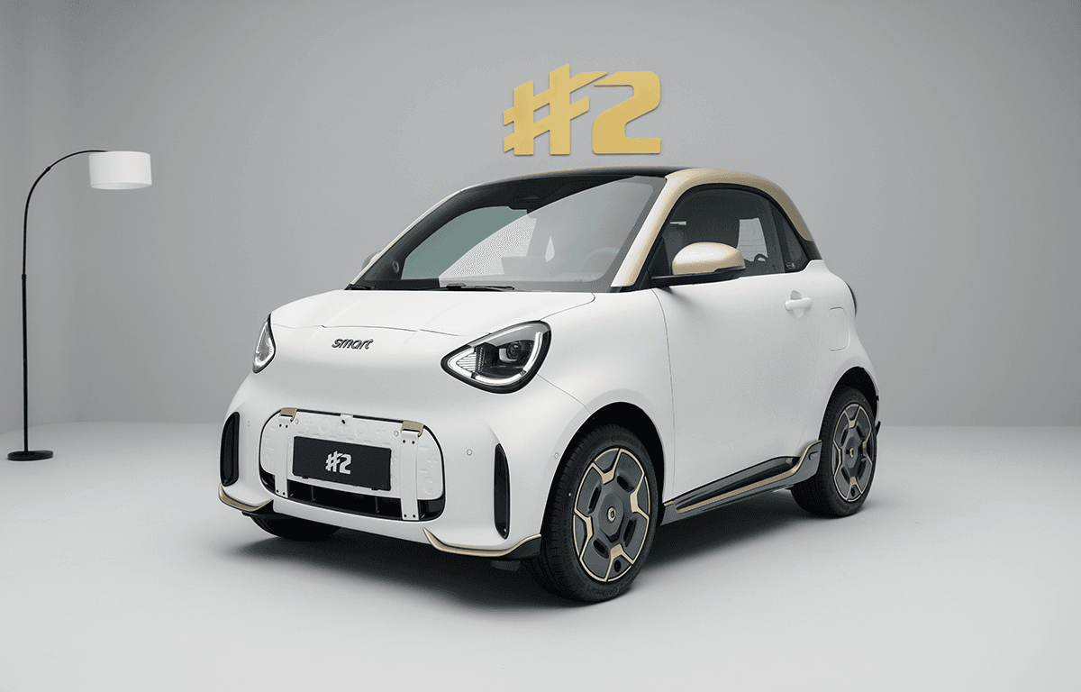 Weißer smart #2 Couture Edition mit goldfarbenem Dach, goldenen Designdetails und markanten Leichtmetallfelgen in der Front- und Seitenansicht vor grauem Hintergrund.