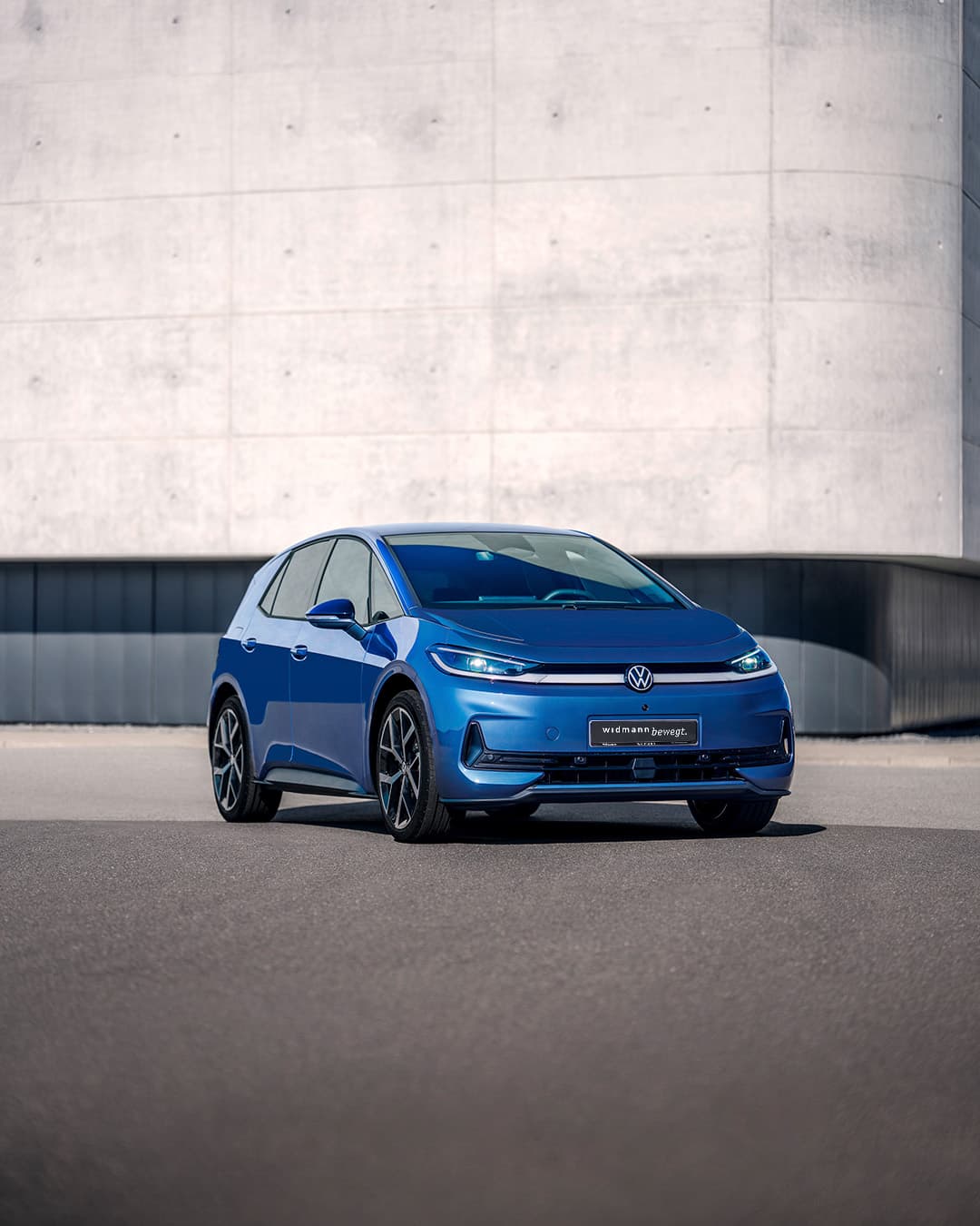 Ein blauer Volkswagen steht auf einer freien Fläche vor einer großen, schlichten Betonwand.