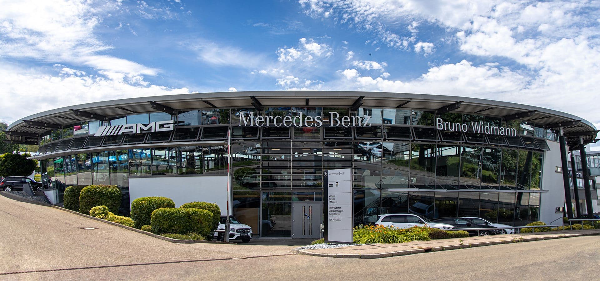 Das Bild zeigt unser Mercedes-Benz Autohaus von außen, vor dem mehrere Fahrzeuge geparkt sind.