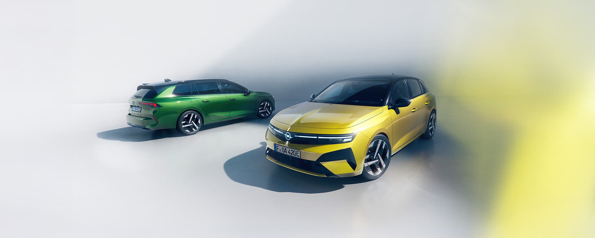 Gelber Opel Astra und grüner Opel Astra Sports Tourer in moderner Studio-Umgebung.