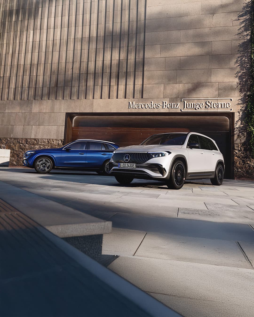 Zwei Mercedes-Benz Junge Sterne, eines in blau und eines in weiß, stehen vor einem modernen Gebäude