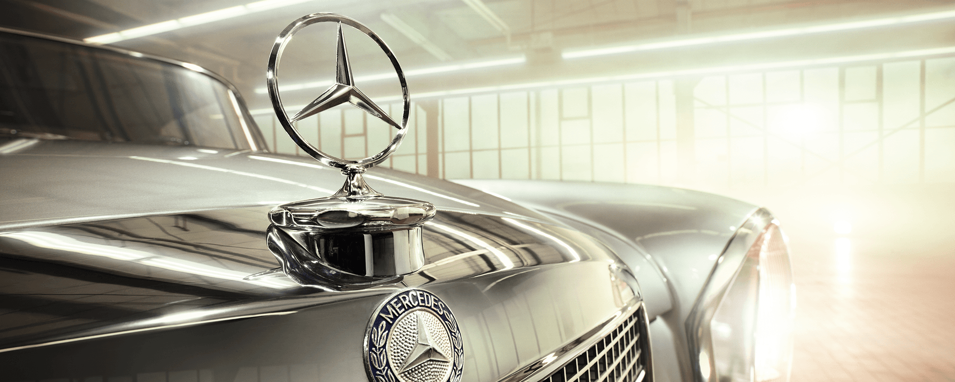 Nahaufnahme eines klassischen Mercedes-Benz mit glänzender Motorhaube und Stern-Emblem in heller Werkhalle.