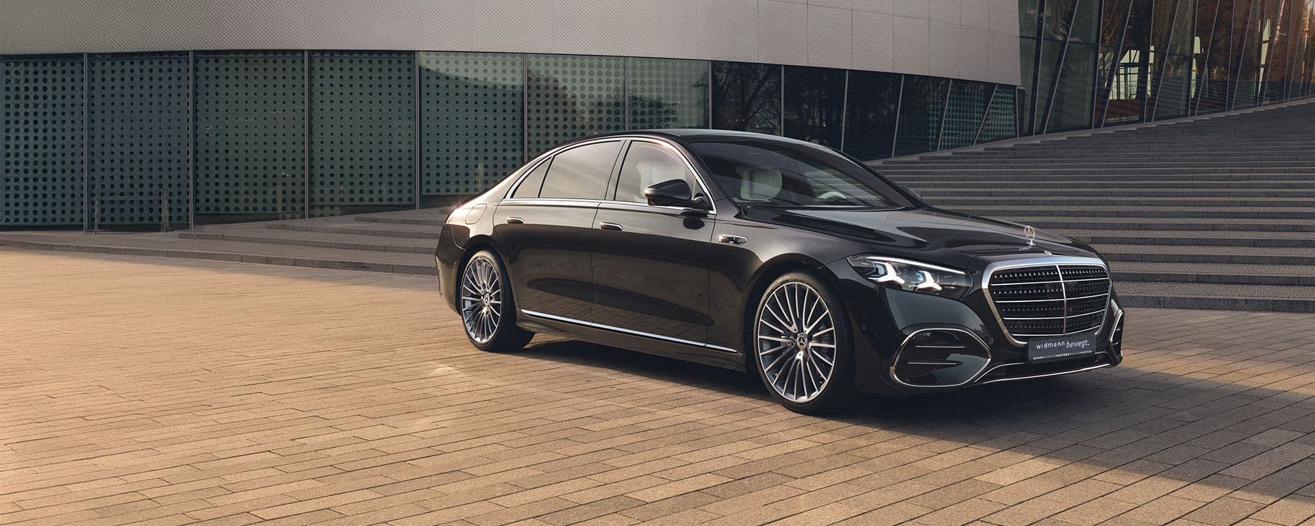 Eine schwarze S-Klasse steht vor einem modernen Gebäude mit breiten Stufen.
