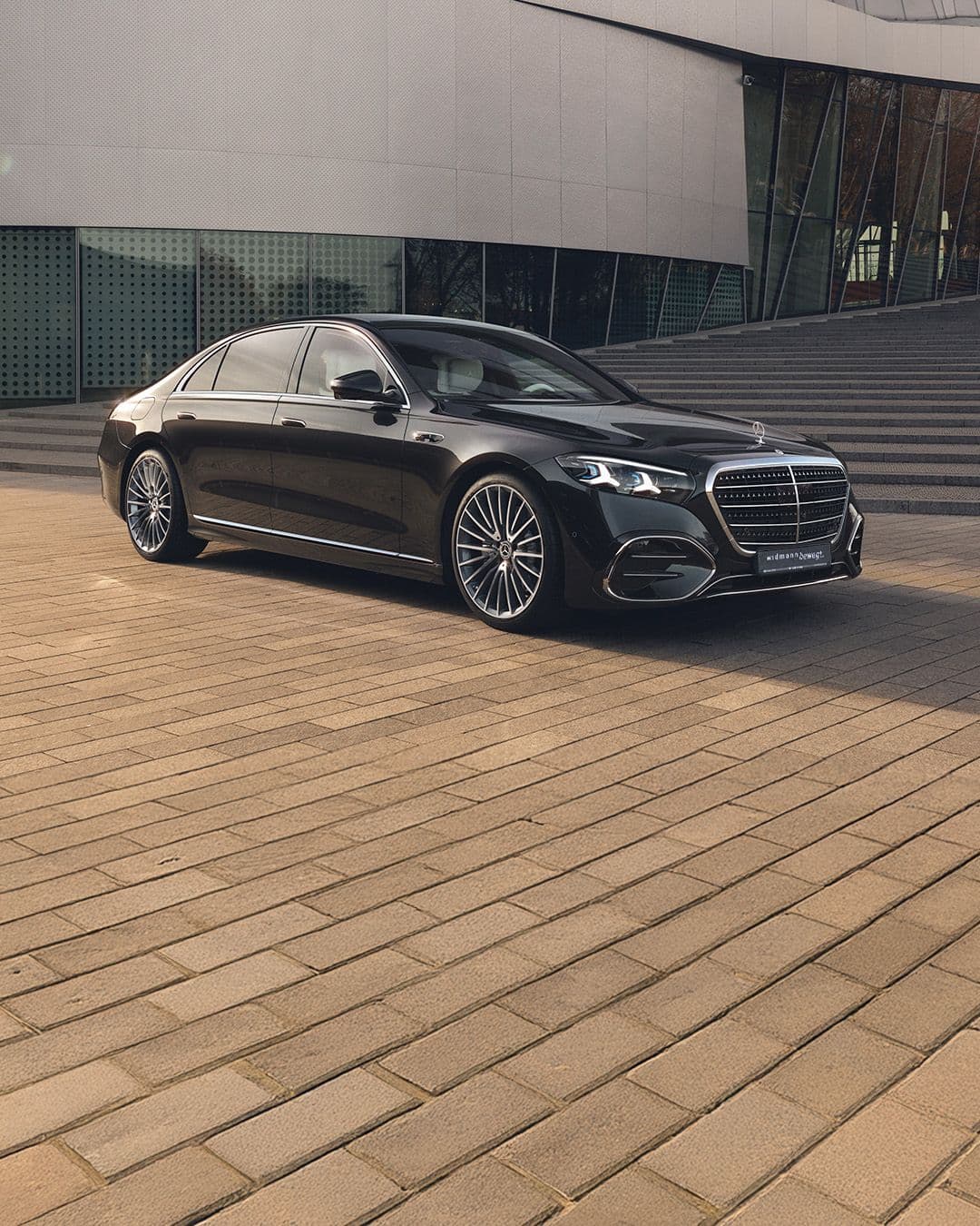 Eine schwarze S-Klasse steht vor einem modernen Gebäude mit breiten Stufen.
