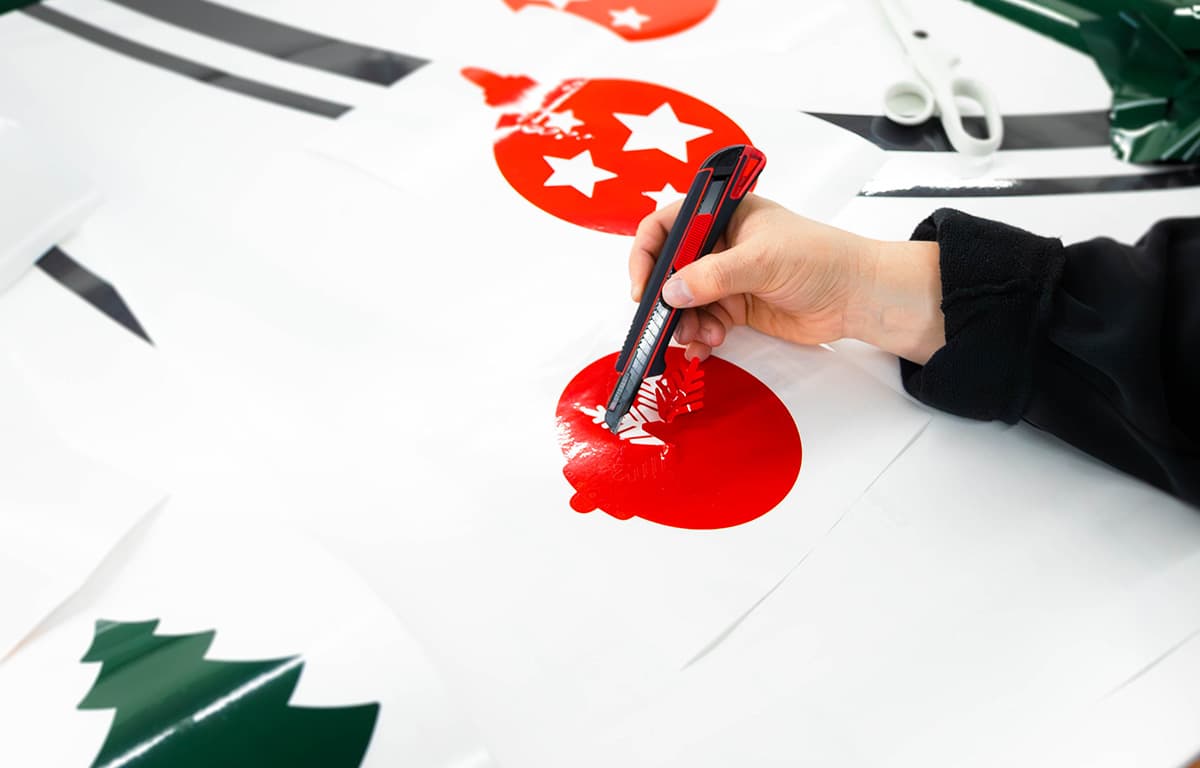 Eine Hand schneidet mit einem Cutter rote Aufkleber mit weißen Sternen aus einer Folie aus.