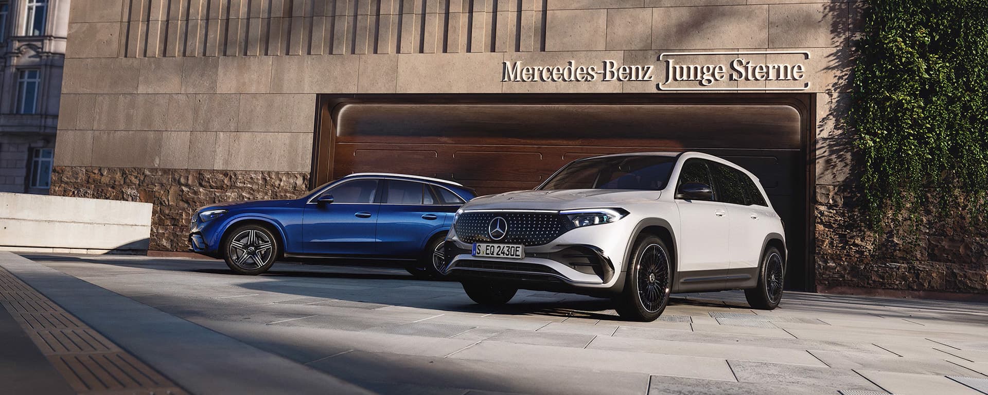 Zwei Mercedes-Benz Junge Sterne, eines in blau und eines in weiß, stehen vor einem modernen Gebäude