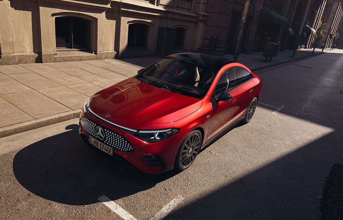 Auf einer Stadtstraße steht ein roter Mercedes-Benz CLA mit schwarzem Dach, von schräg oben fotografiert, neben hellen Gebäudefassaden im Sonnenlicht.