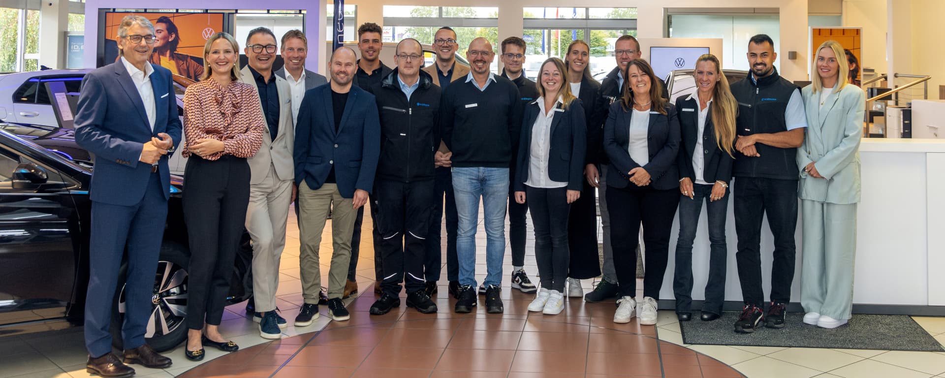 Eine Gruppe von Mitarbeitenden steht in einem Autohaus nebeneinander und lächelt gemeinsam in die Kamera.