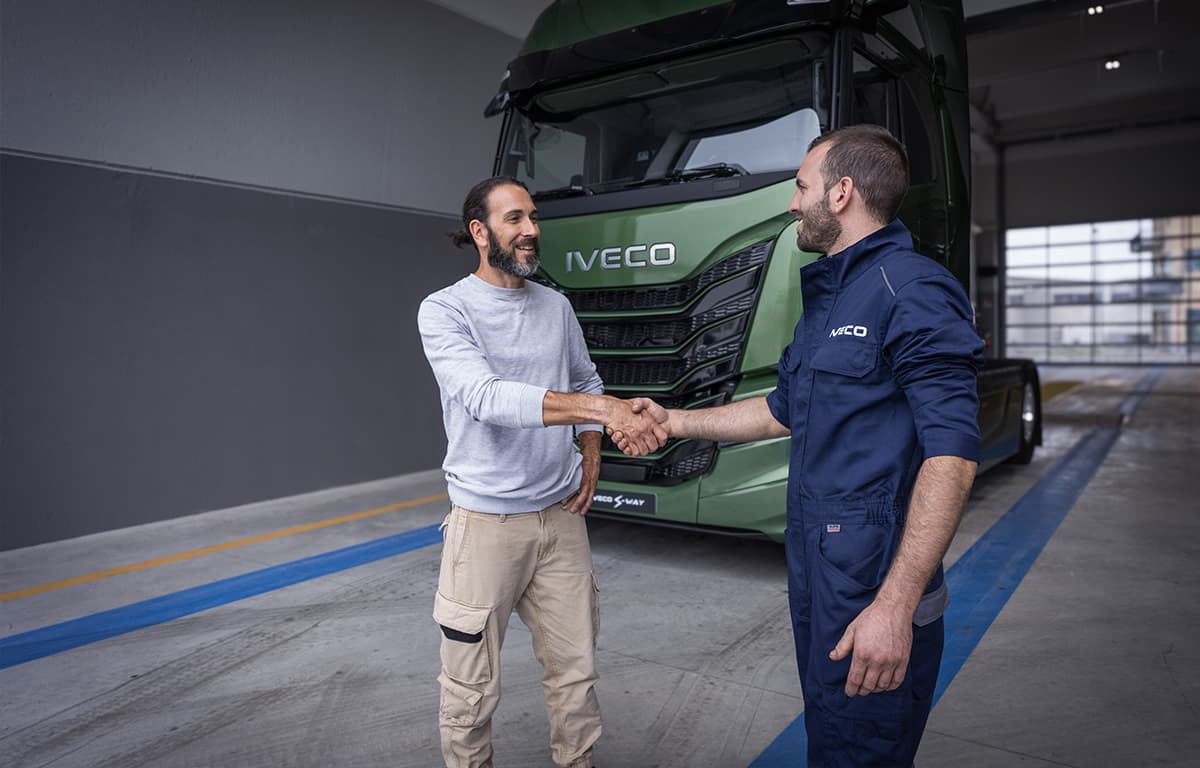 Ein Kunde und ein Werkstattmitarbeiter geben sich die Hand. Im Hintergrund ein IVECO Lkw.