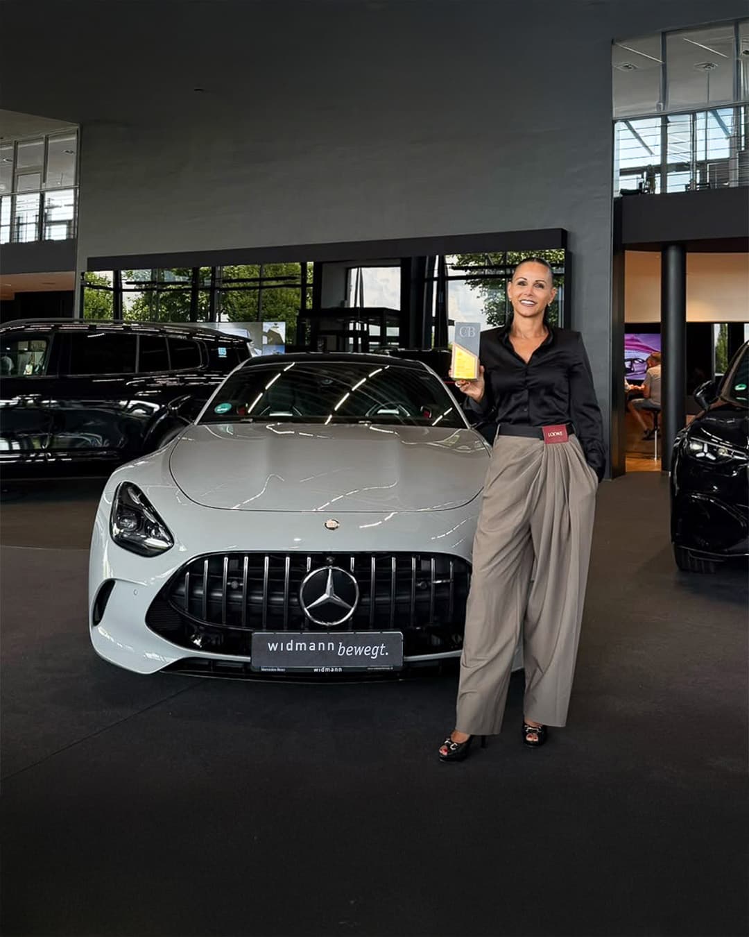 Frau mit Auszeichnung neben zwei Mercedes-Benz Fahrzeugen im Autohaus.