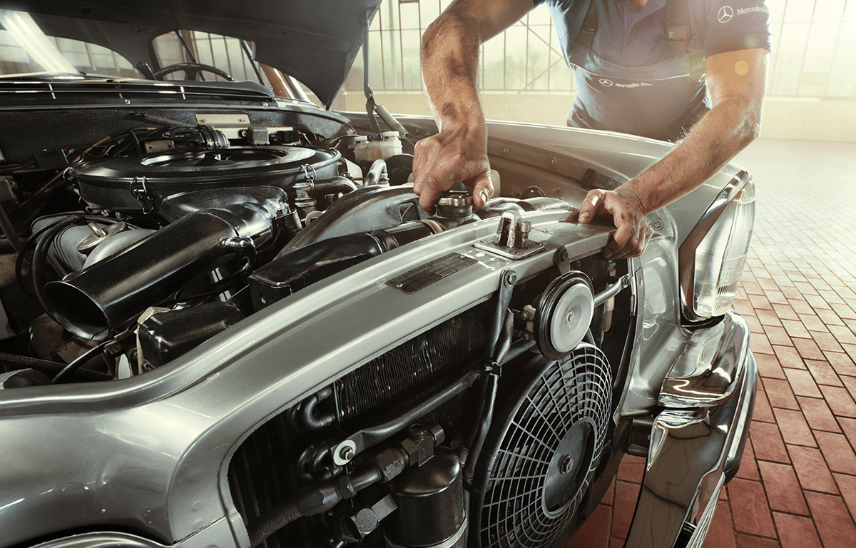 Mechaniker arbeitet am offenen Motor eines klassischen Mercedes-Benz in heller Werkstatt.