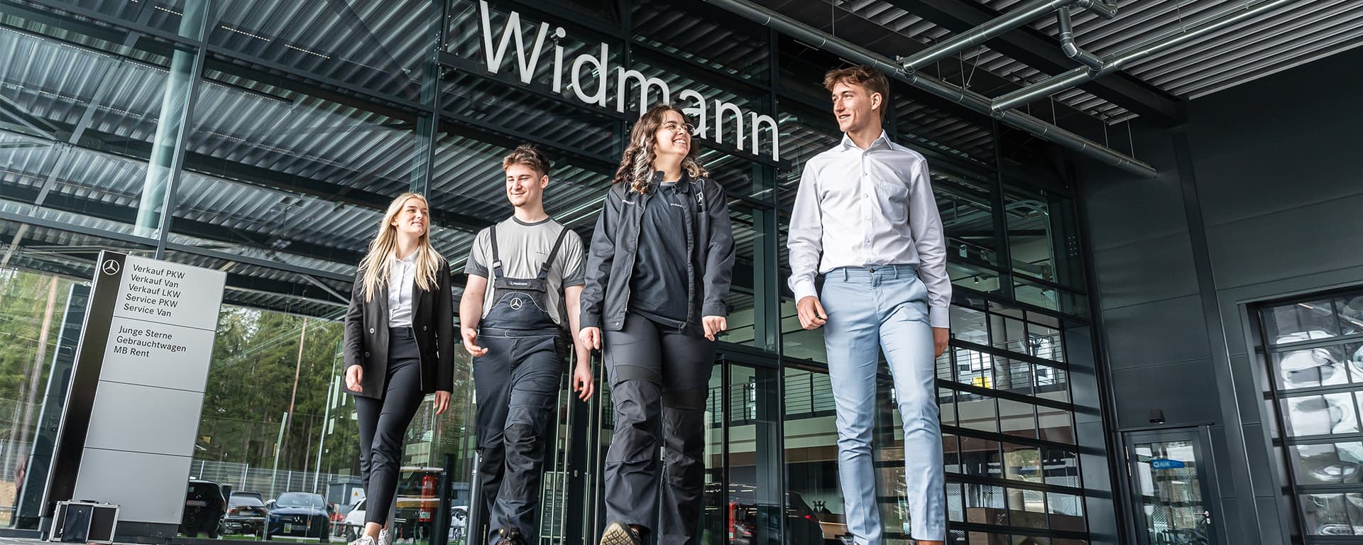 Fünf Mitarbeitende gehen gemeinsam vor dem modernen Glasgebäude von Widmann, dessen Name gut sichtbar über dem Eingang steht.