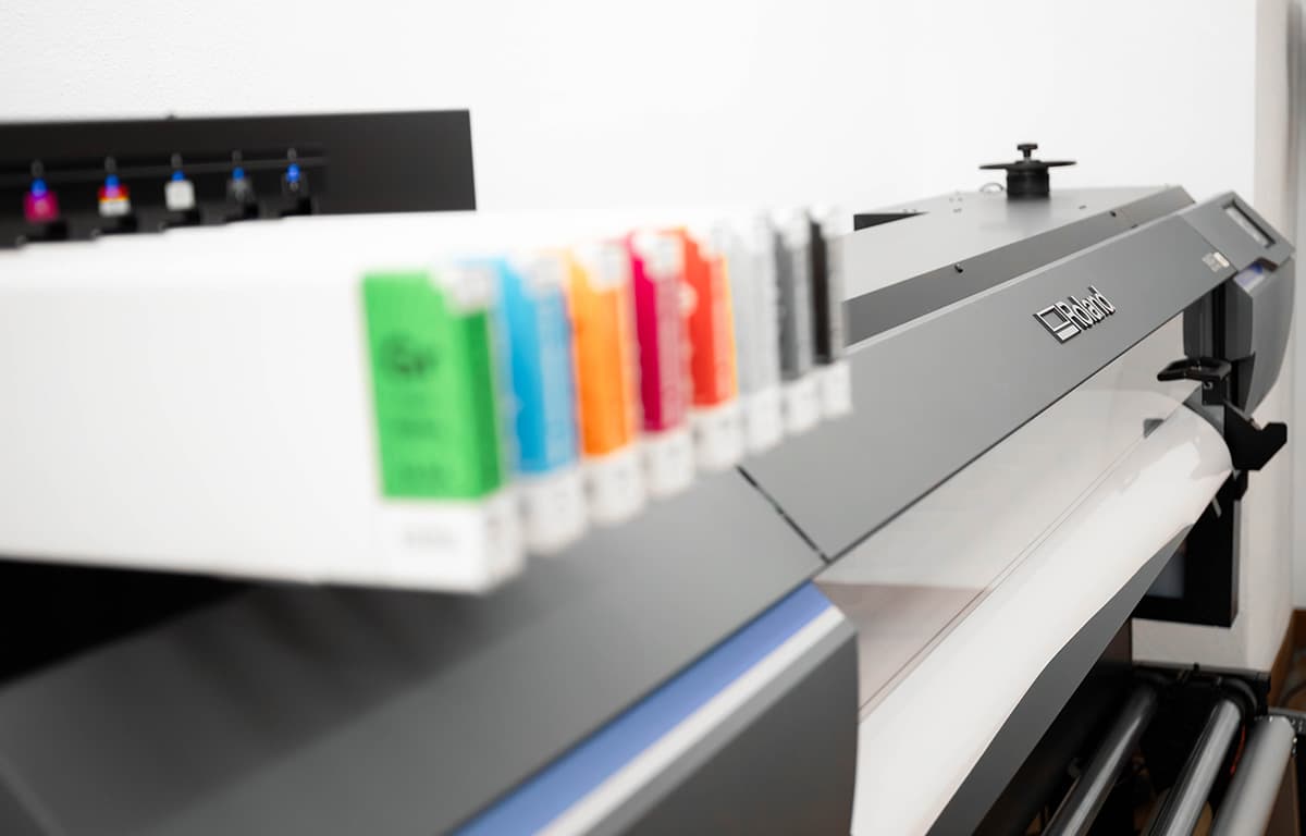 Eine große Druckmaschine mit mehreren farbigen Tintenpatronen steht in einem hellen Arbeitsraum.