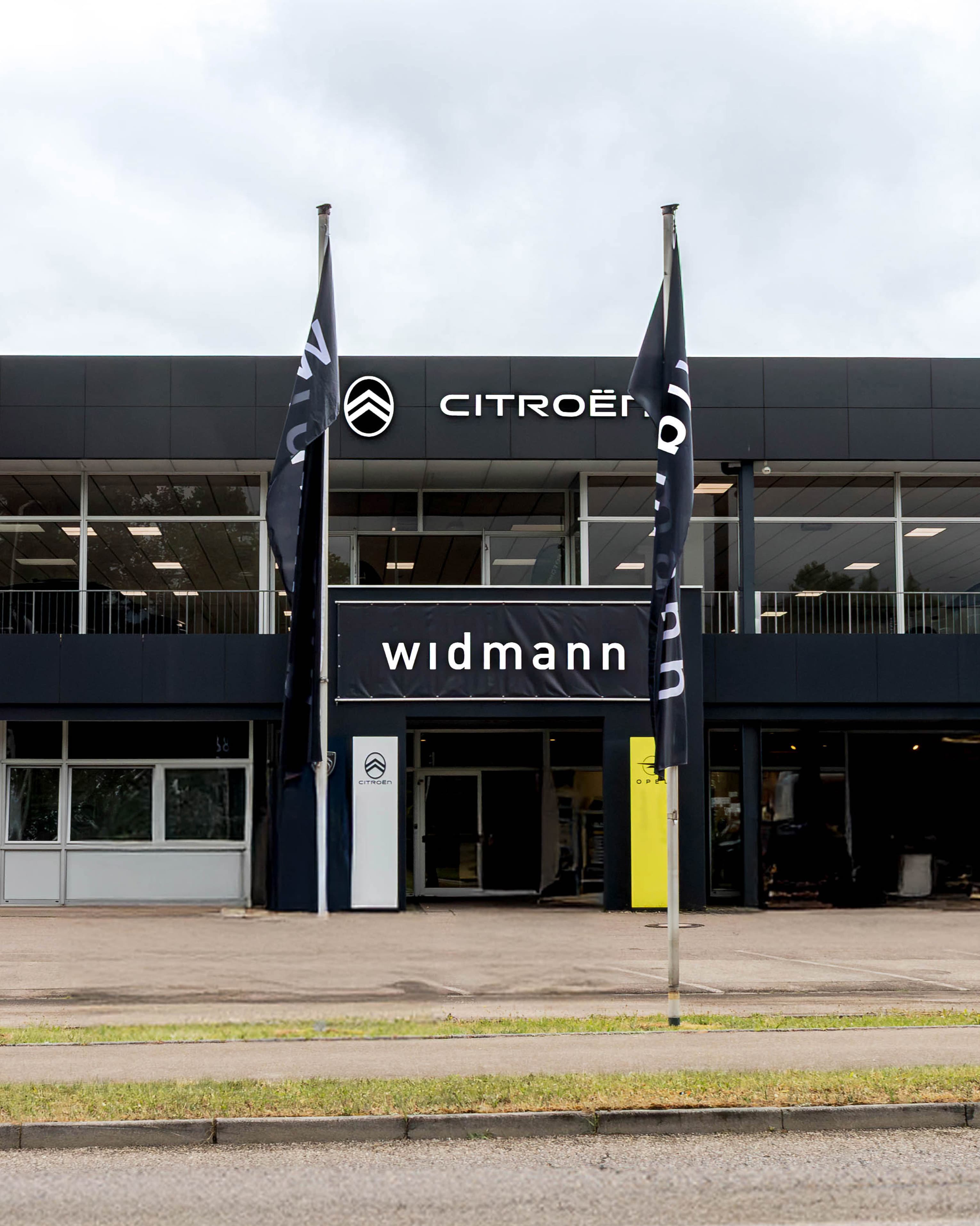 Außenansicht des Autohauses Widmann mit den Marken Peugeot, Citroën und Opel sowie modernem Showroom an einer Straße.