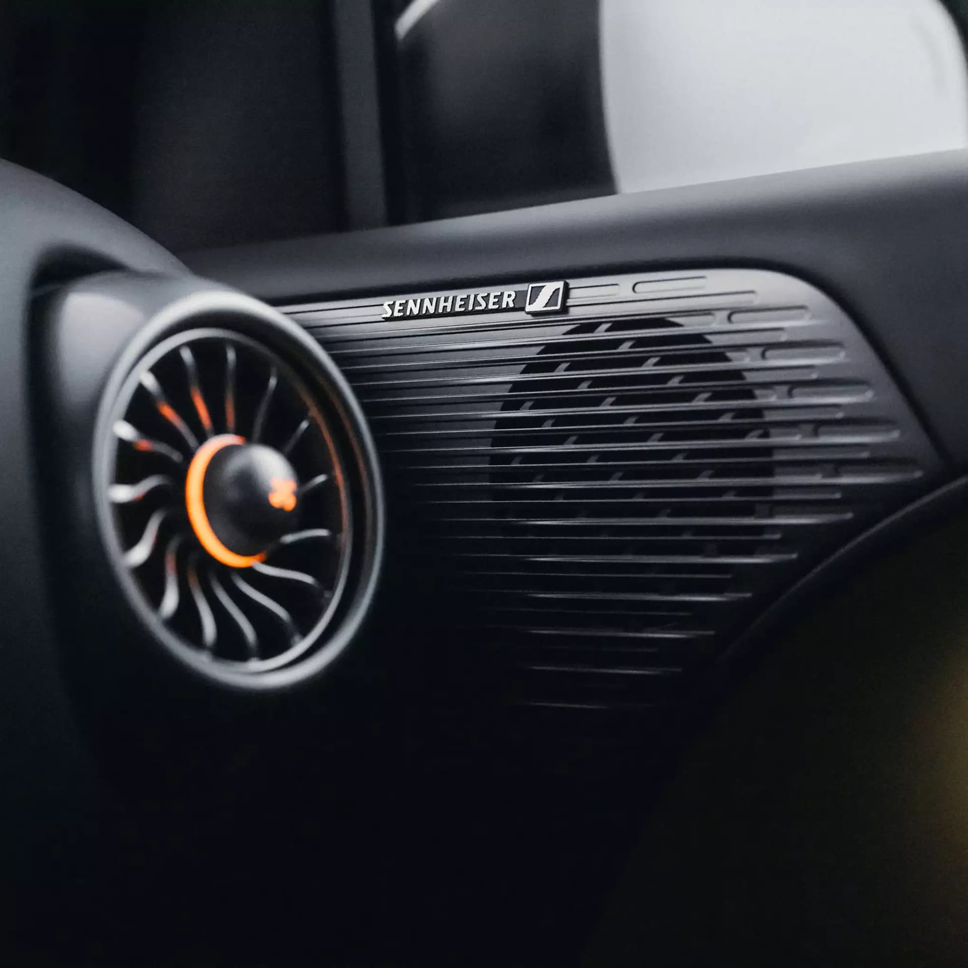 Detailaufnahme des Sennheiser® Lautsprechersystems im smart #2 mit markantem Lautsprechergitter und runder Lüftungsdüse mit orangefarbenen Akzenten.