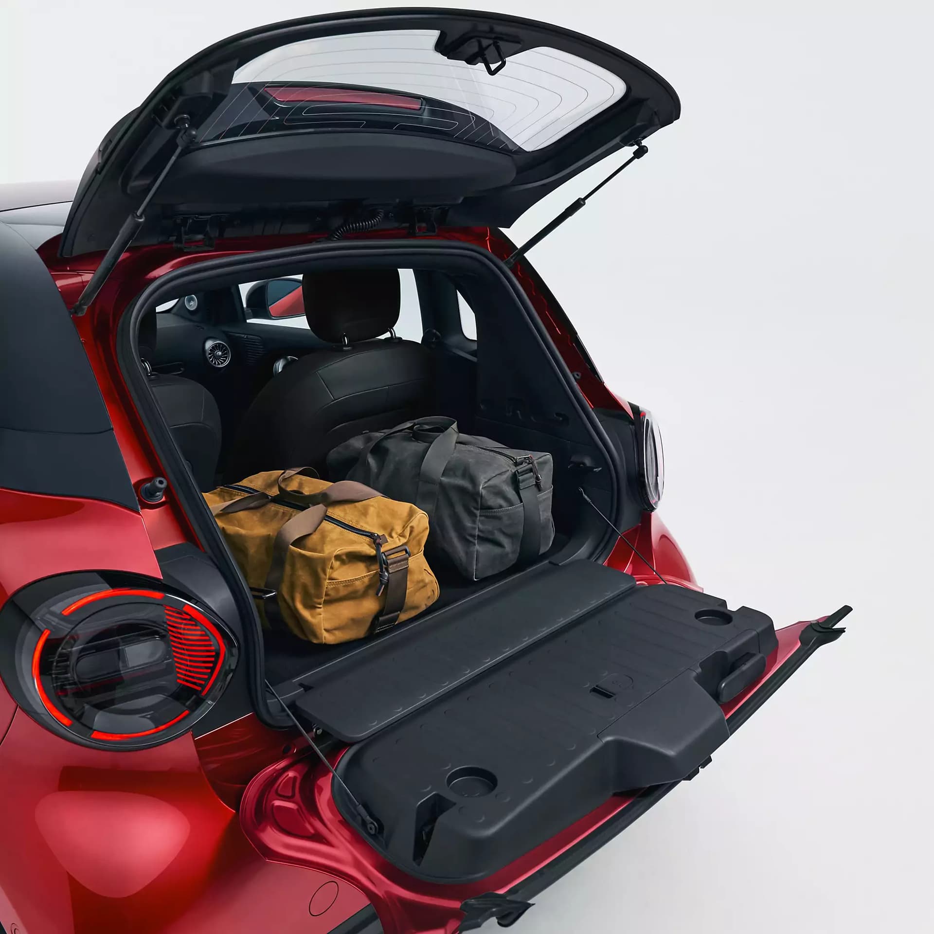 Geöffnete, zweigeteilte Heckklappe eines roten smart #2 mit zwei Reisetaschen im Kofferraum und heruntergeklappter unterer Ladefläche.