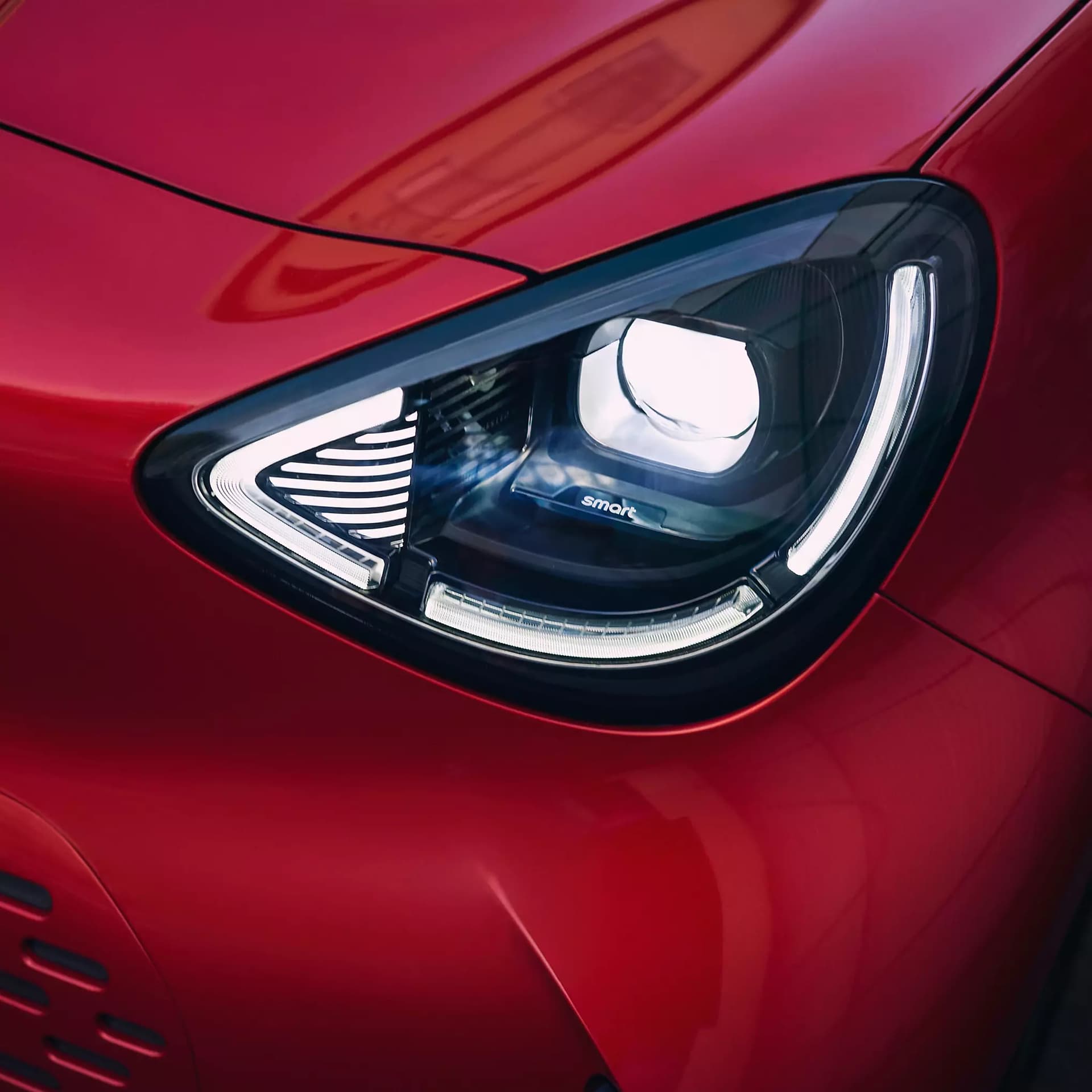 Detailaufnahme des beleuchteten LED-Scheinwerfers eines roten smart #2 mit markanter Lichtsignatur und integriertem smart-Schriftzug.