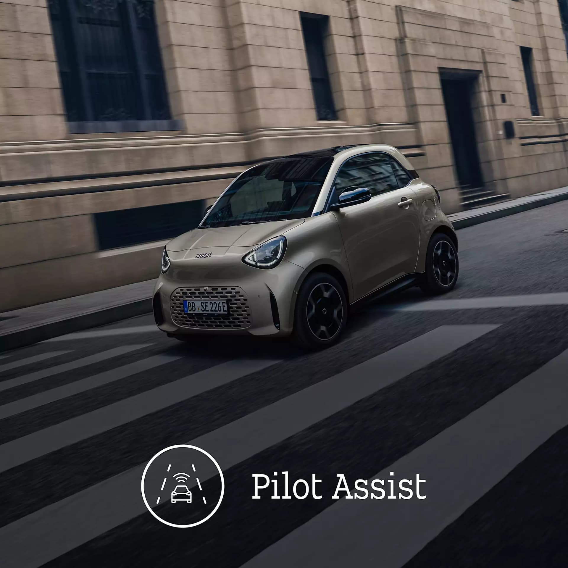 Silberfarbener smart #2 bei der Fahrt durch eine städtische Straße mit Zebrastreifen, ergänzt durch den Hinweis auf das Fahrerassistenzsystem „Pilot Assist“.