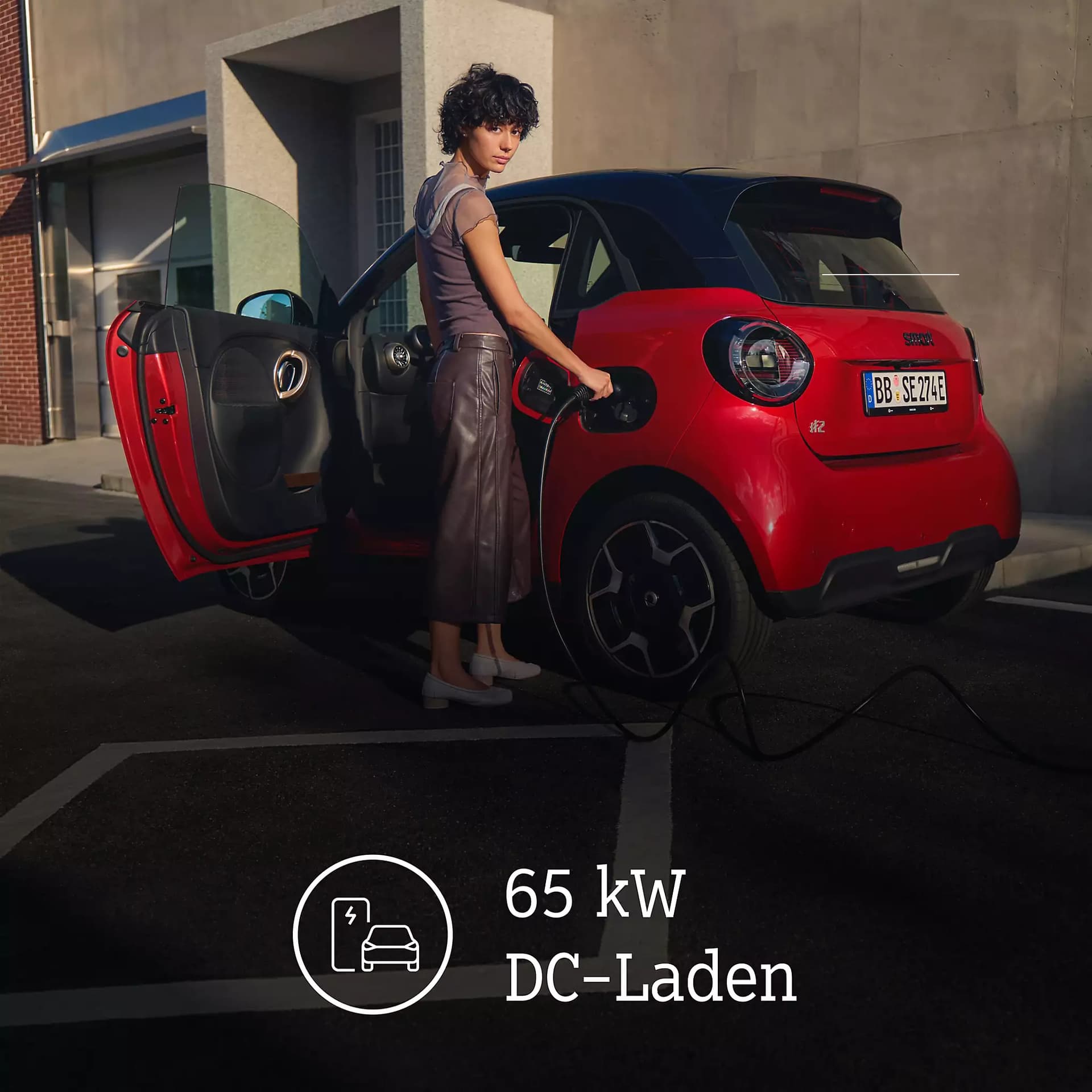 Frau beim Laden eines roten smart #2 mit schwarzem Dach und geöffneter Fahrertür, ergänzt durch den Hinweis auf 65 kW DC-Schnellladen.